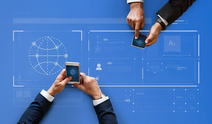 Three business professionals collaborate over a blue board with holographic charts, a globe diagram, and smartphones in their hands.